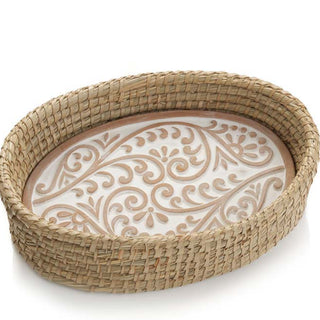 A photo of a bread warmer that is a terra cotta stone in a oval shape with a white washed swirls and dots on it, in a kaisa grass basket. 
