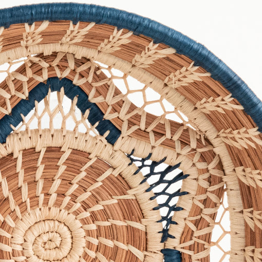 A close-up photo of the Florinda basket, which is a handwoven basket made in Guatemala out of Pine Needles stitched with raffia in both natural and blue shades to create a central six-pointed star motif at the base of the Florinda Basket.