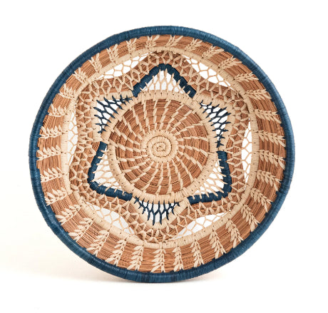 A photo of the Florinda basket, which is a handwoven basket made in Guatemala out of Pine Needles stitched with raffia in both natural and blue shades to create a central six-pointed star motif at the base of the Florinda Basket.