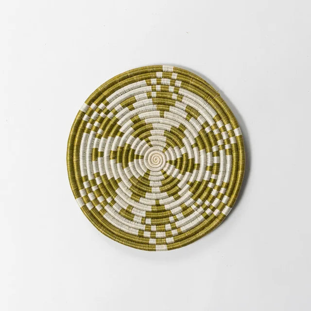 A photo of a trivet made from grass in Rwanda. This one is a grassy green color with a cream white in a kaleidoscope design. 