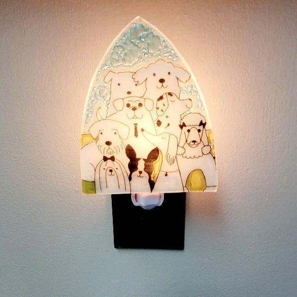 A photo of a nightlight made of recycled glass in Ecuador. This night light features a pack of dogs of different breeds all together in black and white with a blue and green background. 