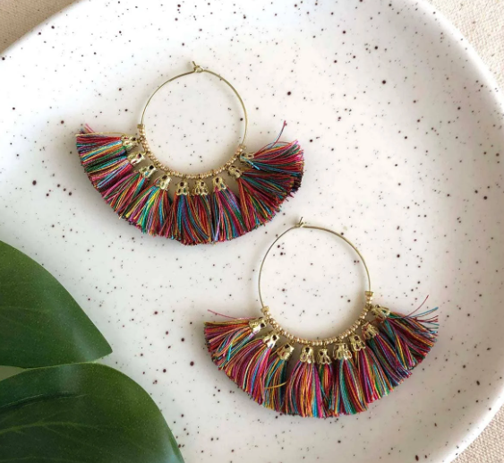 A photo of a pair of earrings that are hoops with dangling tassels of sari fabric in rainbow colors from India. 