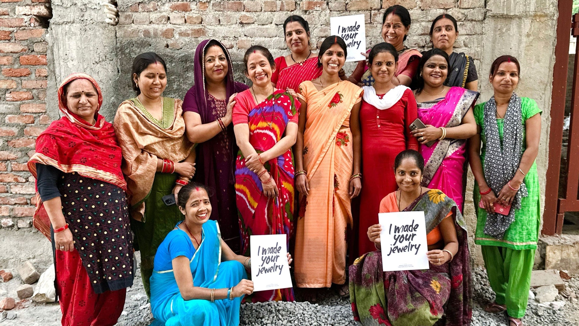 Image of women holding up signs saying "I Made Your Jewelry" for World HeARTs Fair Trade