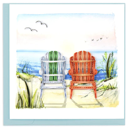 A photo of an intricately quilled greeting card made in Vietnam. This card features a pair of Adirondack chairs sitting on a beach scene. 