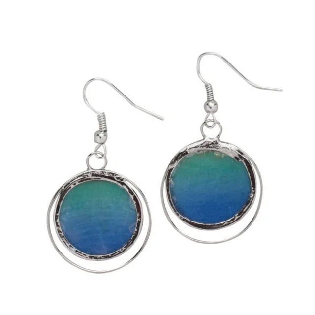 A photo of a pair of earrings made from capiz shells from the Philippines. This one shows the shells in blue ombre circles giving ocean vibes with silver design work and hooks.