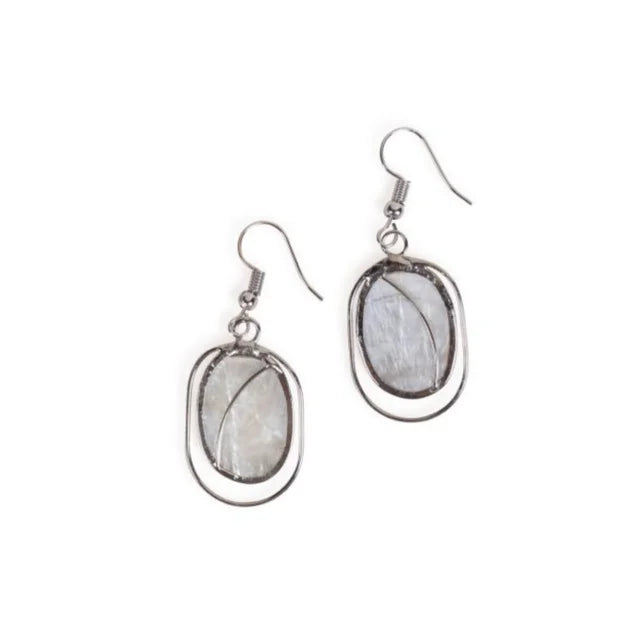 A photo of a pair of earrings made from capiz shells from the Philippines. This one shows the shells in natural white/clear ovals with silver design work and hooks.