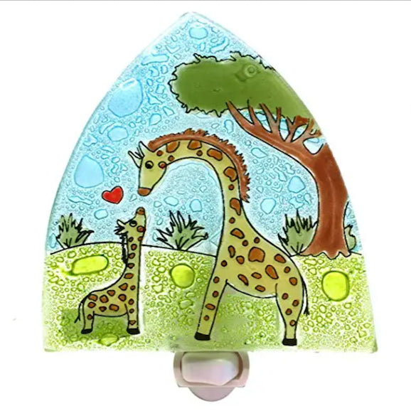 A photo of a nightlight made of recycled glass in Ecuador. This night light features a cartoon giraffe mom and baby with a heart in between and a forest background. 
