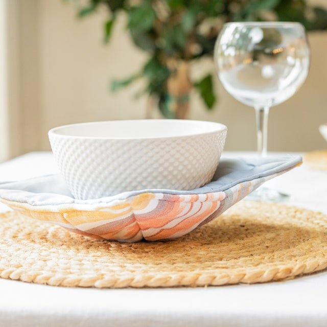 A photo of a bowl in a microwave bowl cozy. This is a colorful textile material that's shape holds a bowl to go in the microwave to keep from your hands touching the hot bowl. Each design is different, and the one pictured has a sedona color tone. 