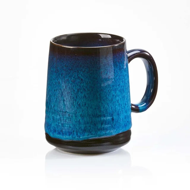 A photo of a Vietnamese mug that showcases a blue color that is supposed to look like Lak Lake, it has a black bottom with a wave effect and a dark rim and handle. 
