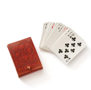 A photo of a leather case with designs of hearts, clubs, diamonds, spades and a deck of cards next to it. 