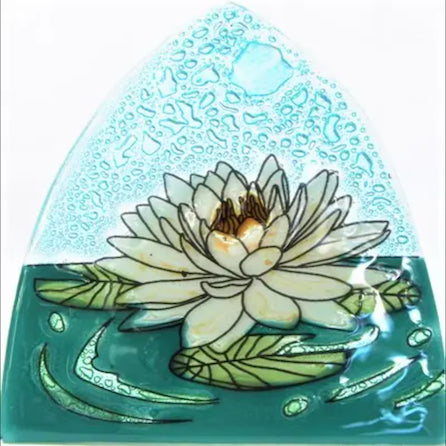A photo of a nightlight made of recycled glass in Ecuador. This night light features a white lotus flower floating in water. 