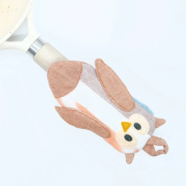 A photo of a owl skillet holder. The photo shows the holder on a pan handle and the little own face with ears and wings forming the shape in neutral owl brown tones. Complete with a hanging loop on top.