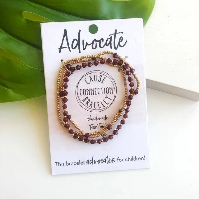 A photo of a trio of Bracelets on a card that says Advocate. This is a set of bracelets that helps advocating for children, by donations with every purchase. These bracelets are a deep red and brass color combo. 