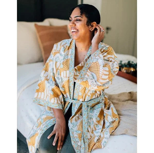 A photo of a model wearing a block-printed robe from India using fair trade values to make this 100% cotton robe. This one is yellow and turquoise patterned with a white background. 