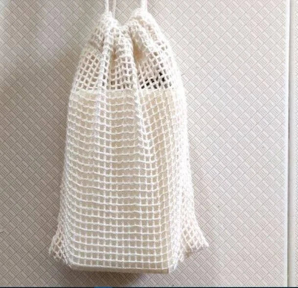 A photo of a white baggie holding a bar of soap. This white baggie is made from cotton and holds soap and is used as a scrubber. 