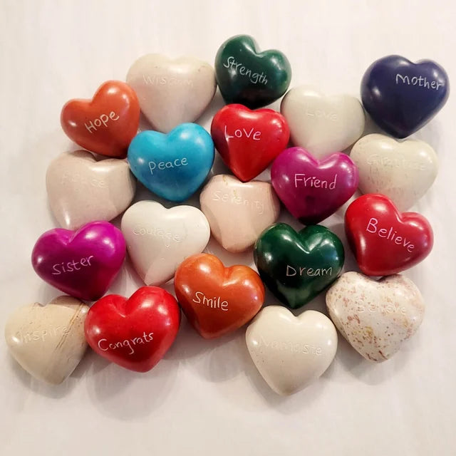 A photo of a variety of soapstone words. Some are natural colors and some are colored brightly. All have words of inspiration on them, like Namaste, Congrats, Inspire, Smile, Strength, Love, Peace, etc. 