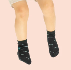 A photo of a model wearing a pair of green kids socks adorned with crocodiles that help save crocodiles through non-profit donations with each purchase of these fair trade socks made in India.