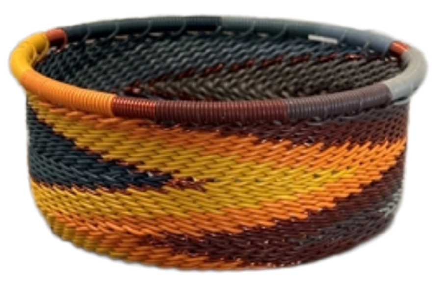 A photo of a small dish that is weaved like a basket made out of telephone wire with colors of oranges, browns, blacks, yellows, and deep reds. 