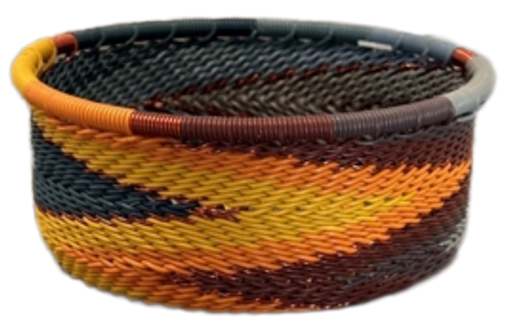 A photo of a small dish that is weaved like a basket made out of telephone wire with colors of oranges, browns, blacks, yellows, and deep reds. 
