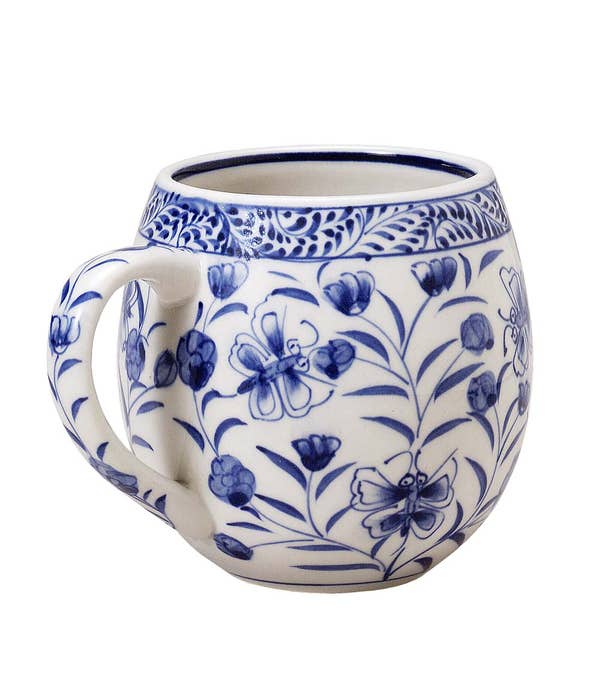 A photo of a Vietnamese mug. The base is white and it has handpainted blue designs of butterflies and flowers covering the outside of the mug. 
