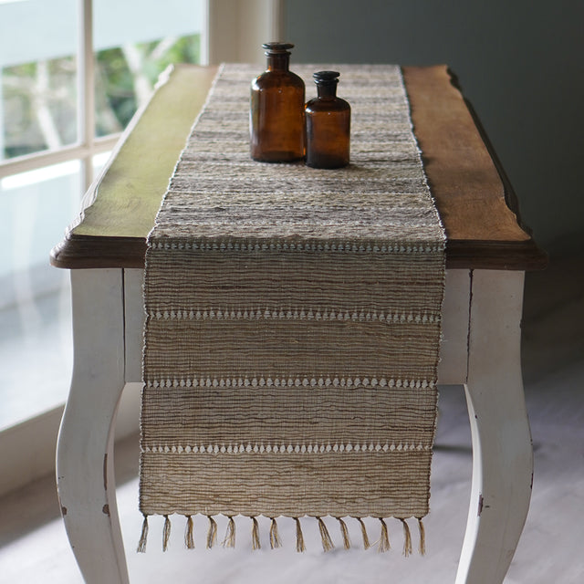 A photo of the Beige table runner from Indonesia. Their is one laying our displayed with beige stripes and tassel ends.